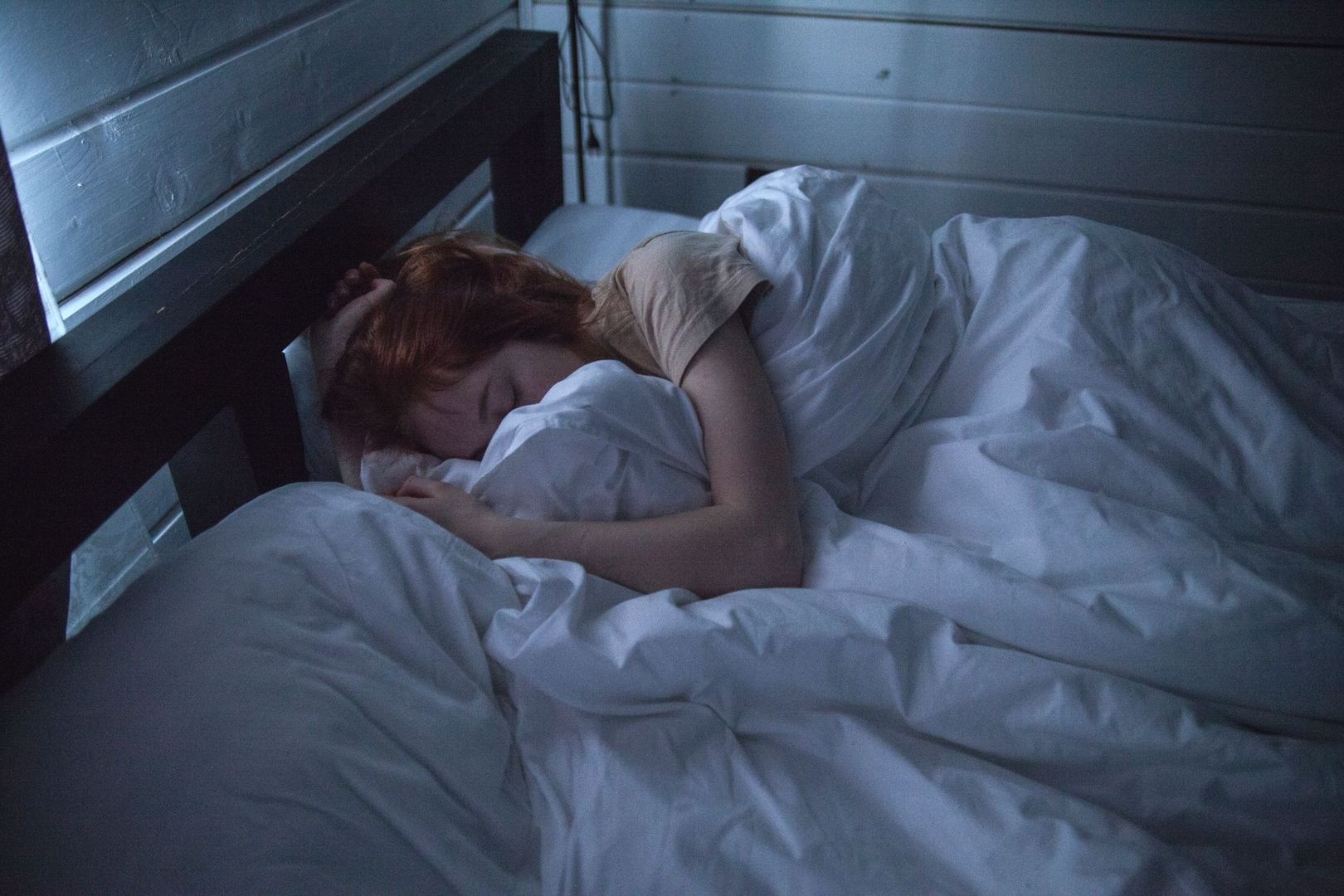 Person som sover under ett vitt täcke i ett mörkt sovrum